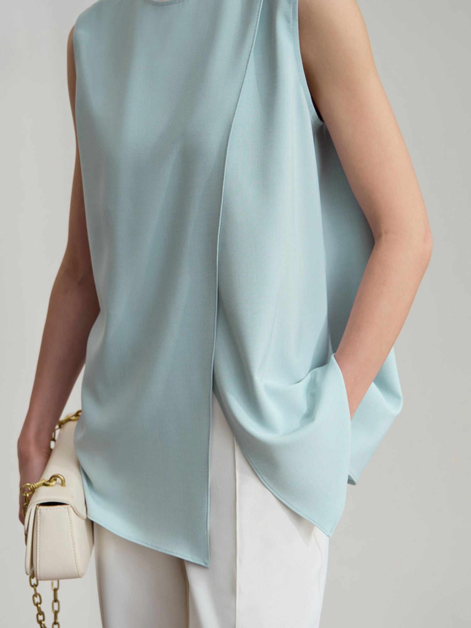 Frau mit hellblauer ärmelloser Bluse und weißer Hose, frontal fotografiert