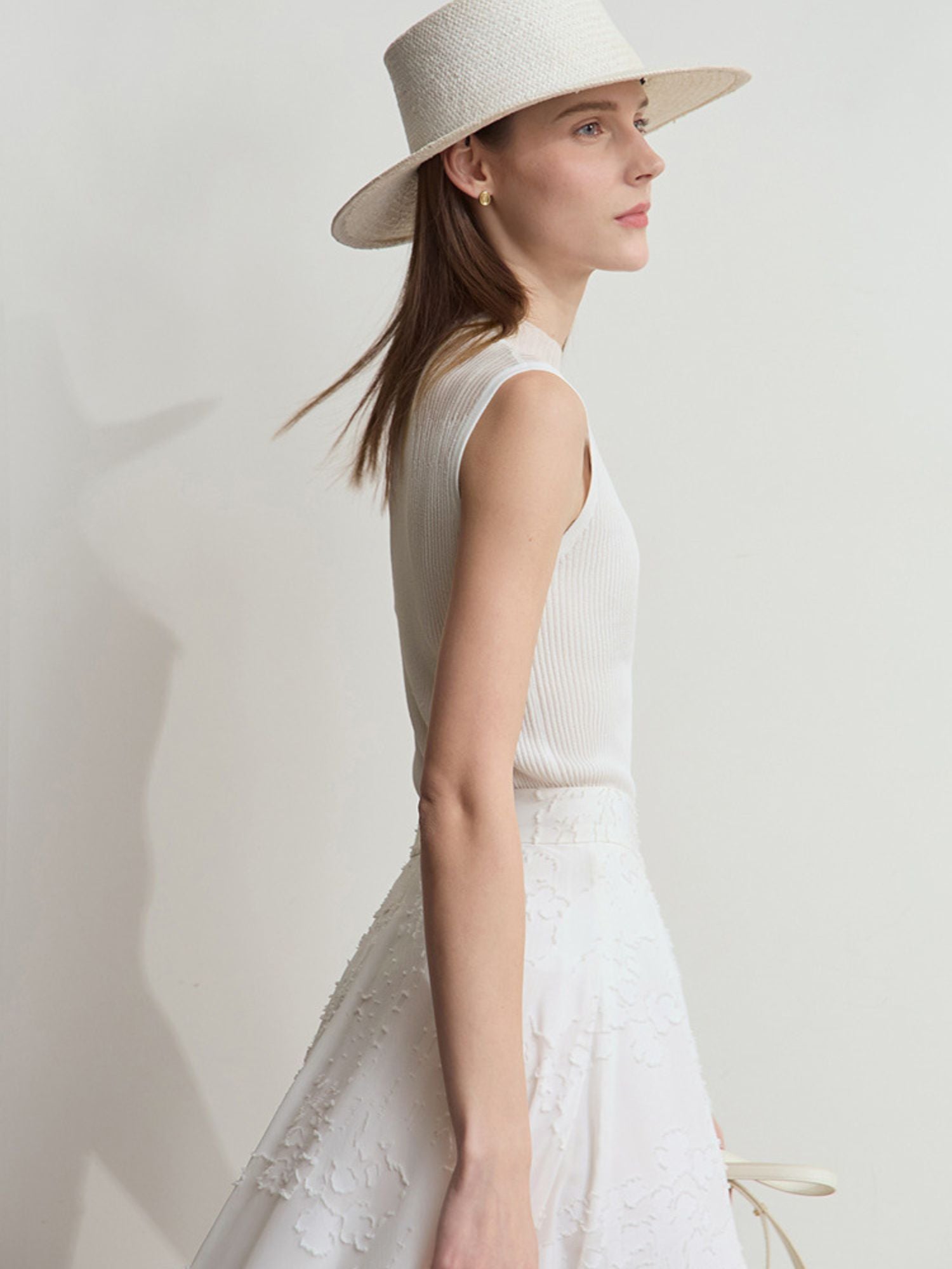 Frau mit cremefarbenem Stricktop, hebt Arm leicht, trägt Sonnenhut