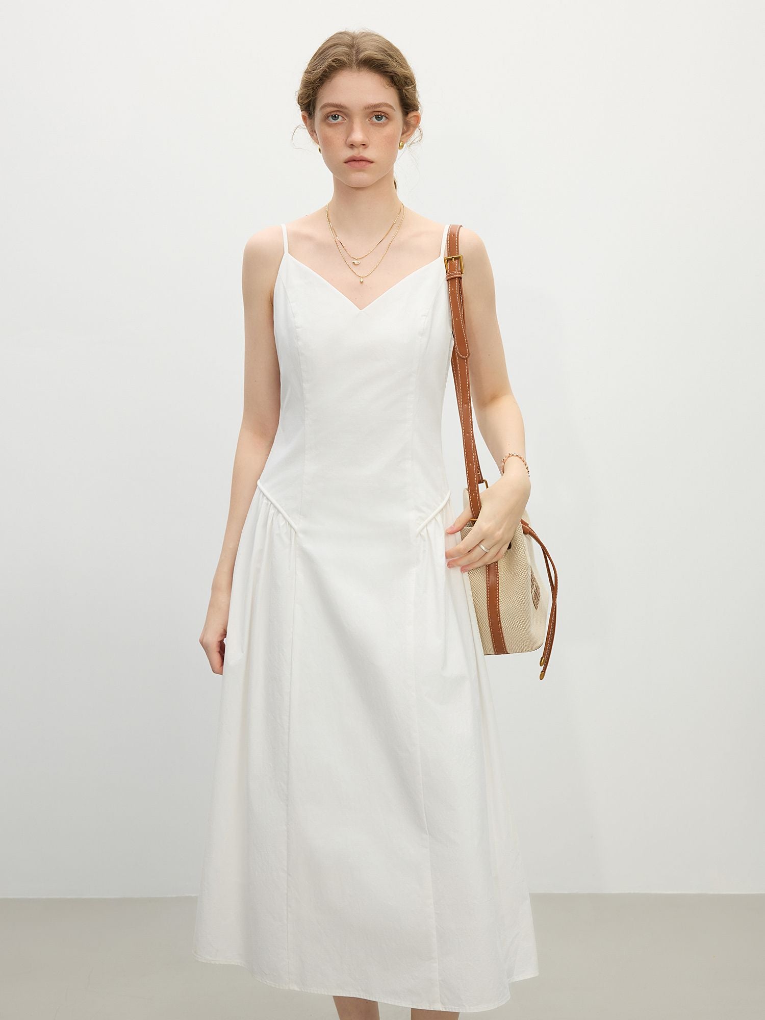 Frau in weißem ärmellosem Kleid mit V-Ausschnitt und Schultertasche, stehend im Studio