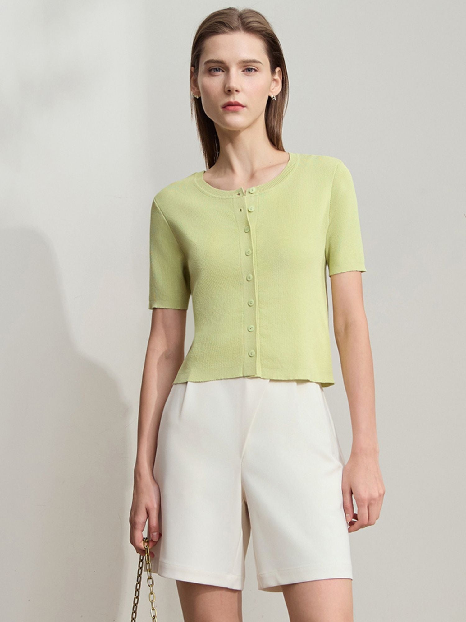 Frau trägt kurzärmliges, hellgrünes Stricktop mit Knopfleiste und weißer Shorts