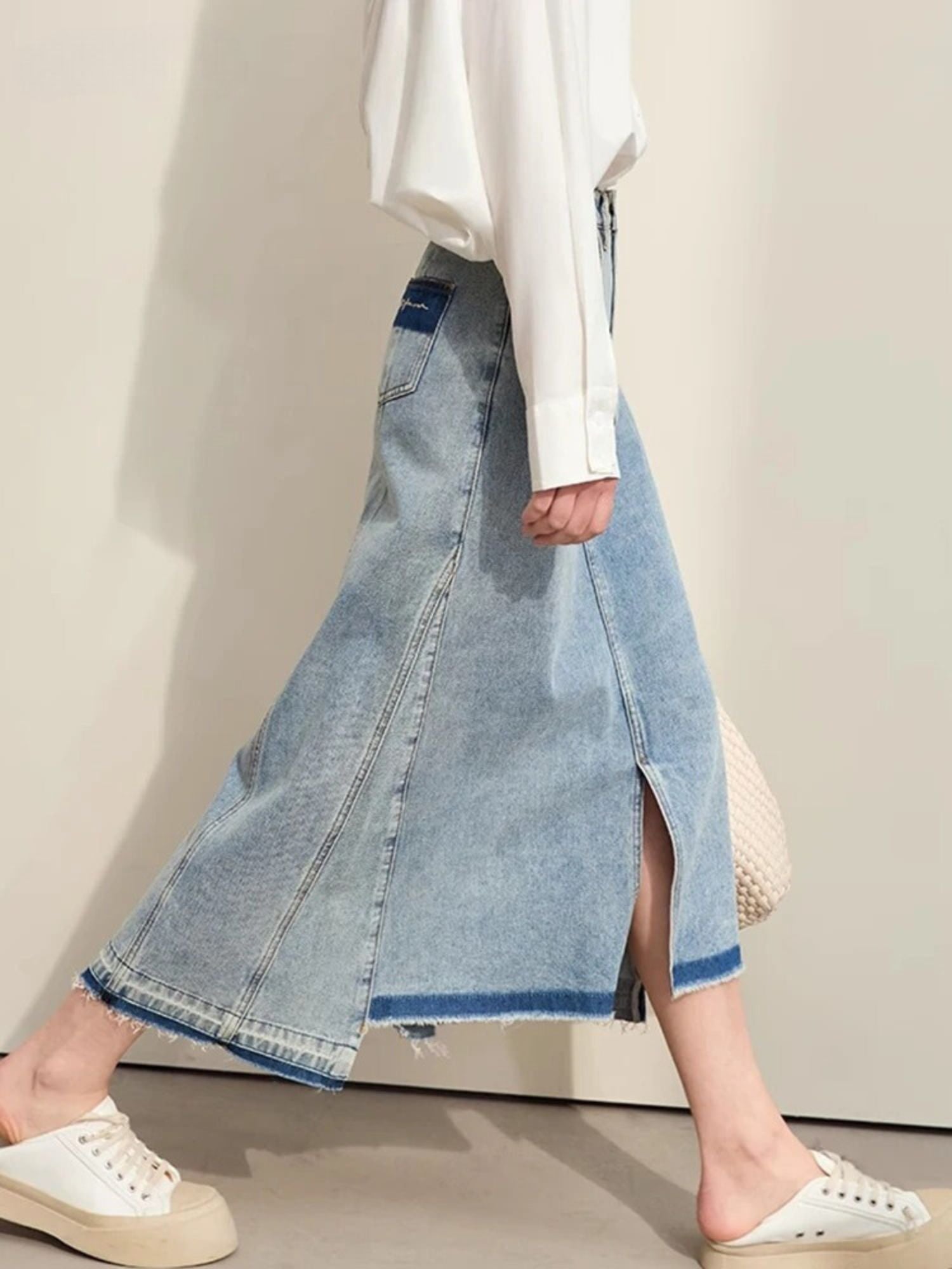 Side view of light-wash denim midi skirt with raw hem, front slit, and sneakers