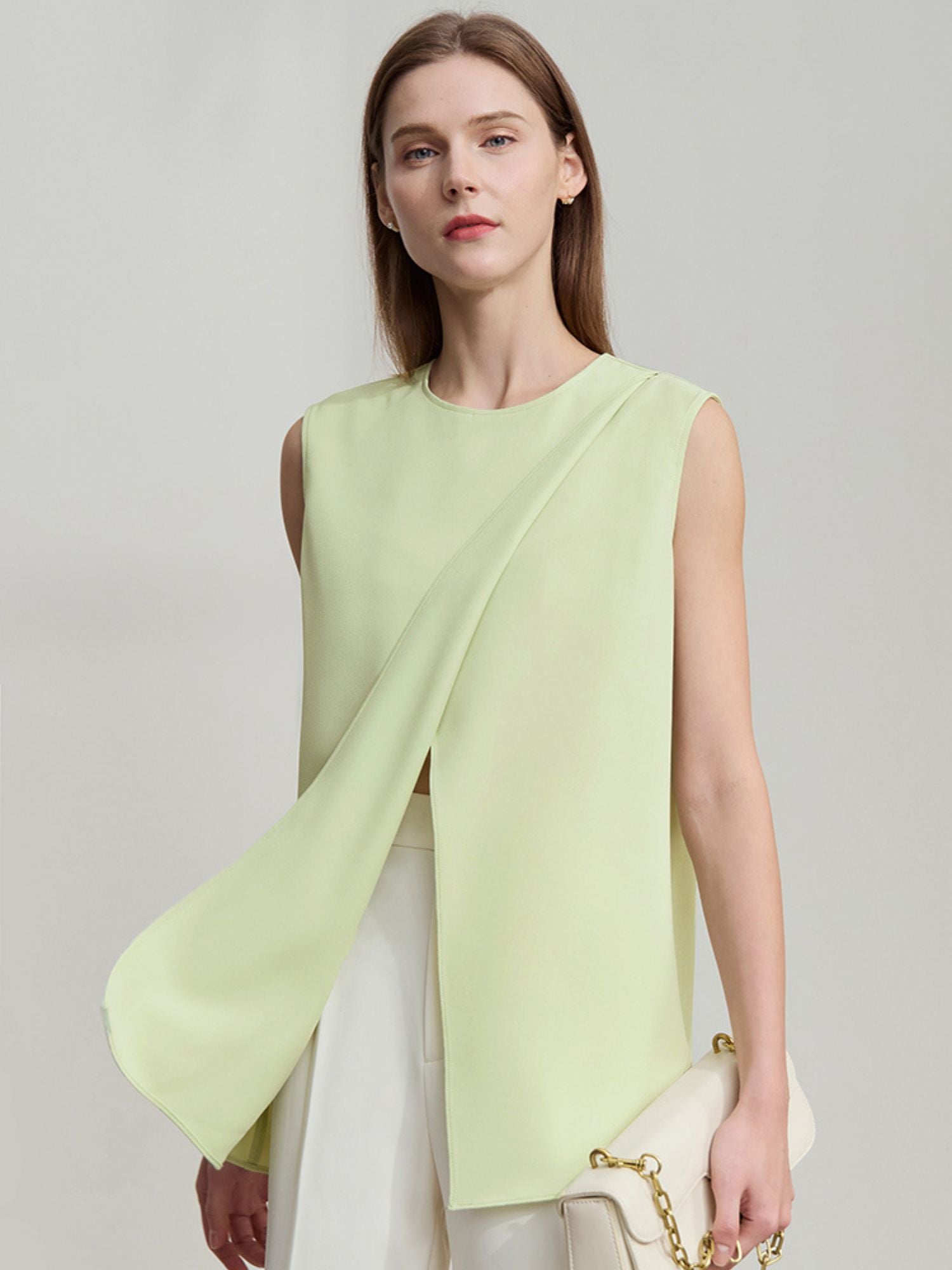 Frau trägt ärmellose hellgrüne Bluse mit asymmetrischem Schnitt und weißer Hose