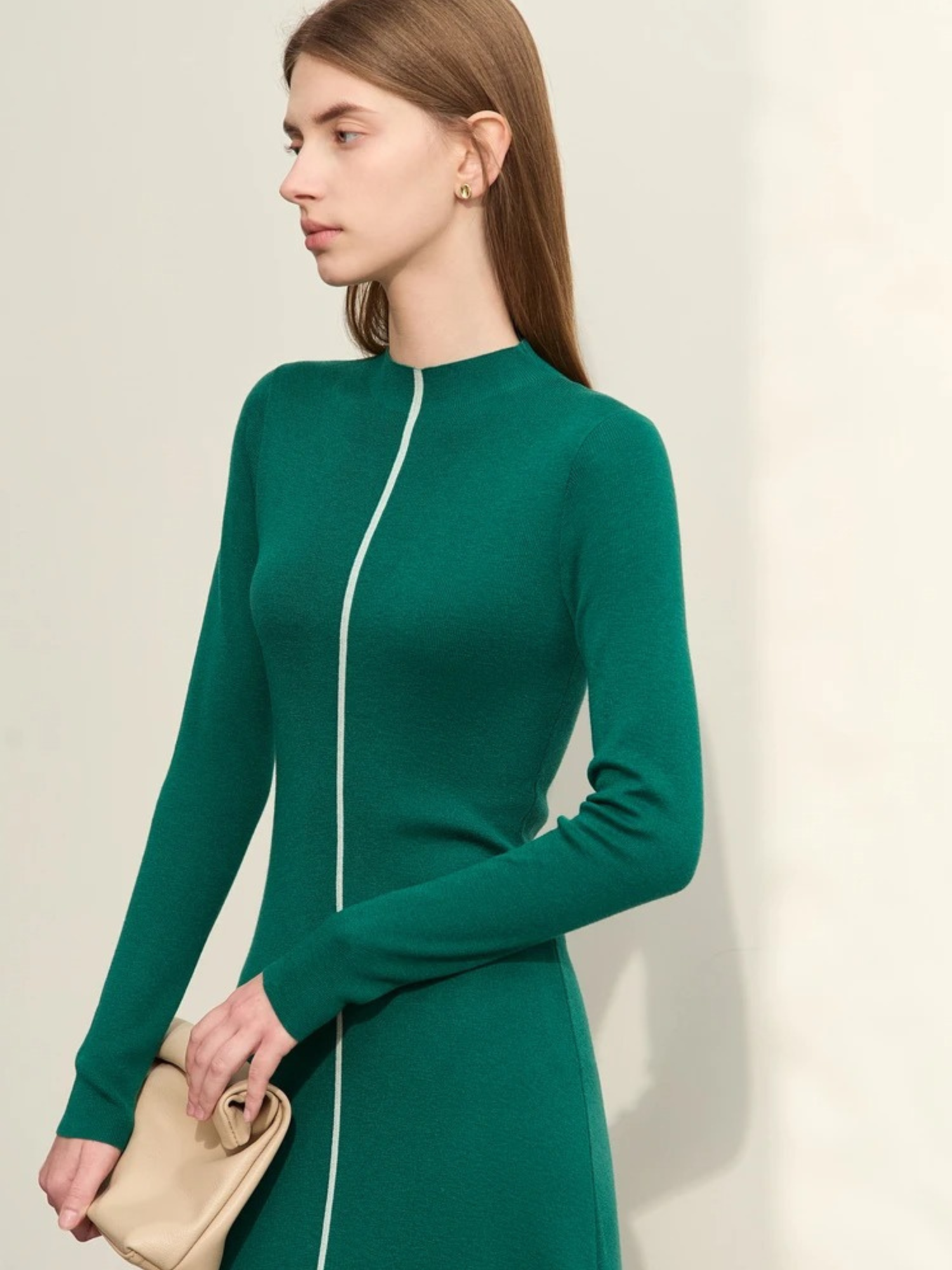 Side profile of green zip-up ribbed dress with long sleeves and cream clutch