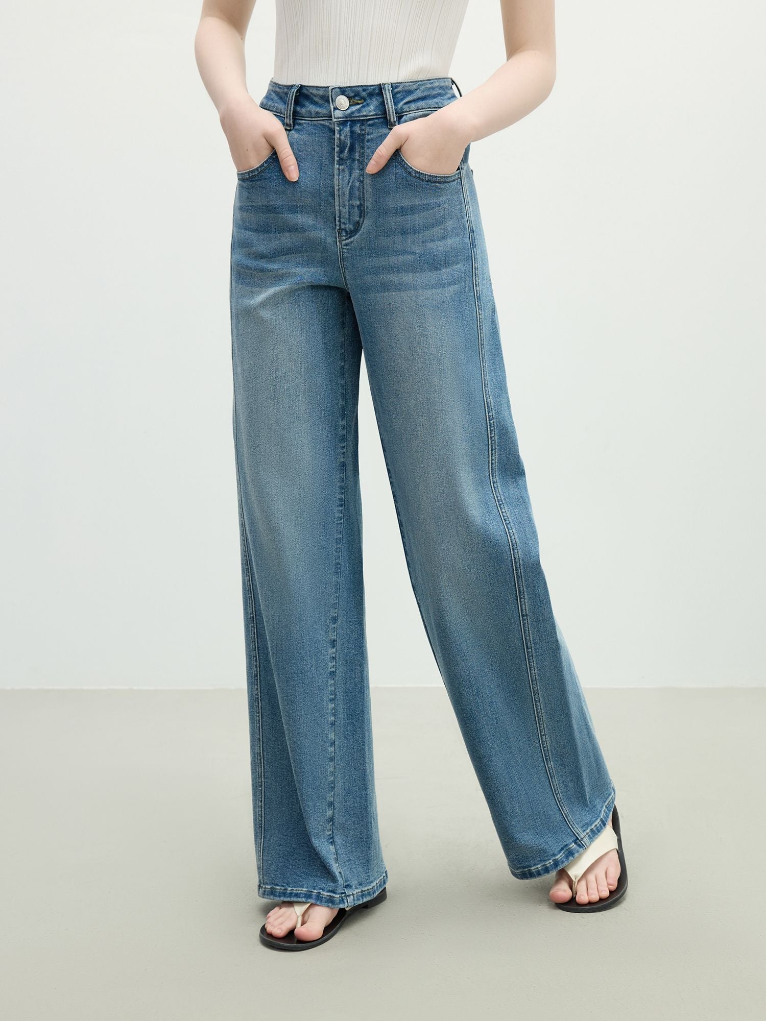 Weit geschnittene blaue Jeans mit mittelhohem Bund, frontal getragen mit offenen Schuhen