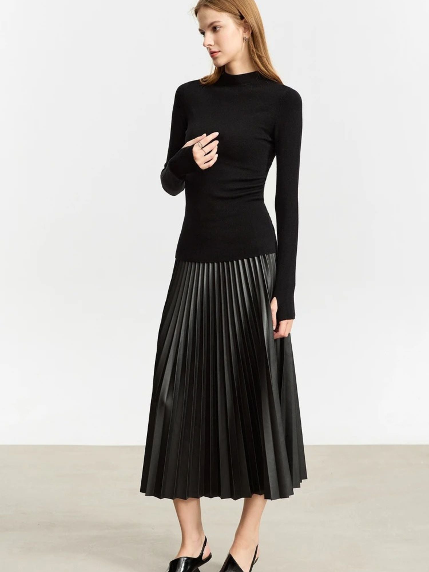 Front view of black pleated skirt with soft shine, paired with long-sleeve black top