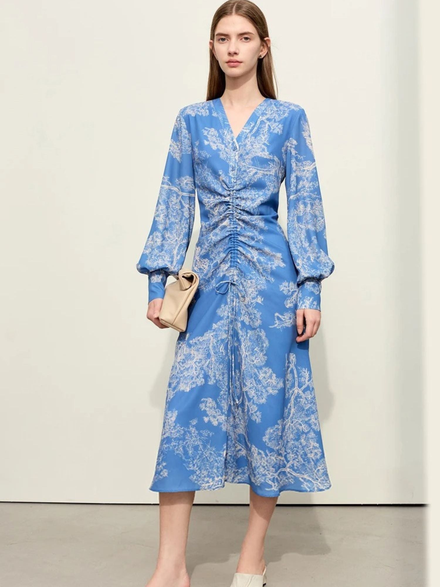 Full-length view of ruched blue floral dress with puff sleeves and neutral handbag