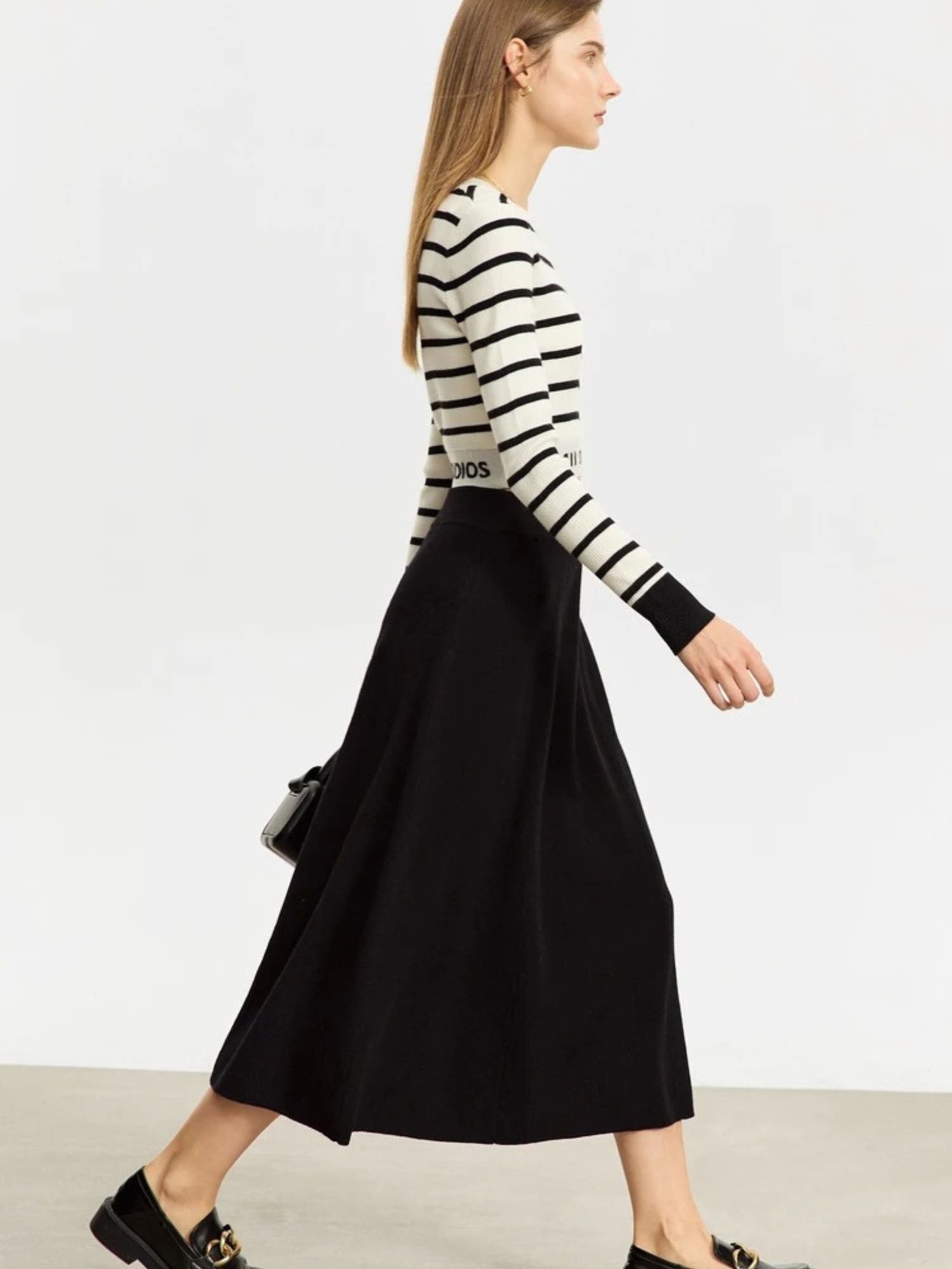 Side profile of black flared midi skirt paired with striped top and loafers