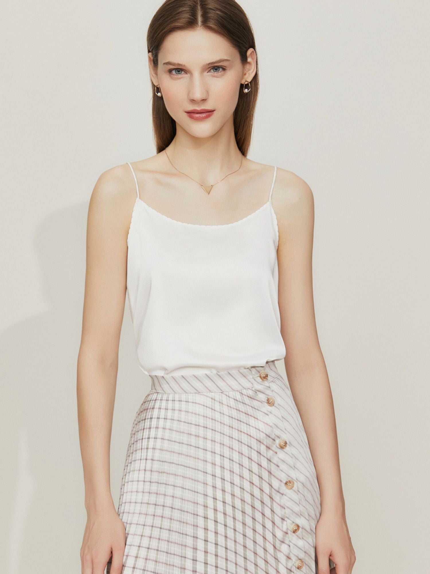 Frau trägt weißes Spaghettiträger-Top mit glänzender Oberfläche und kariertem Faltenrock