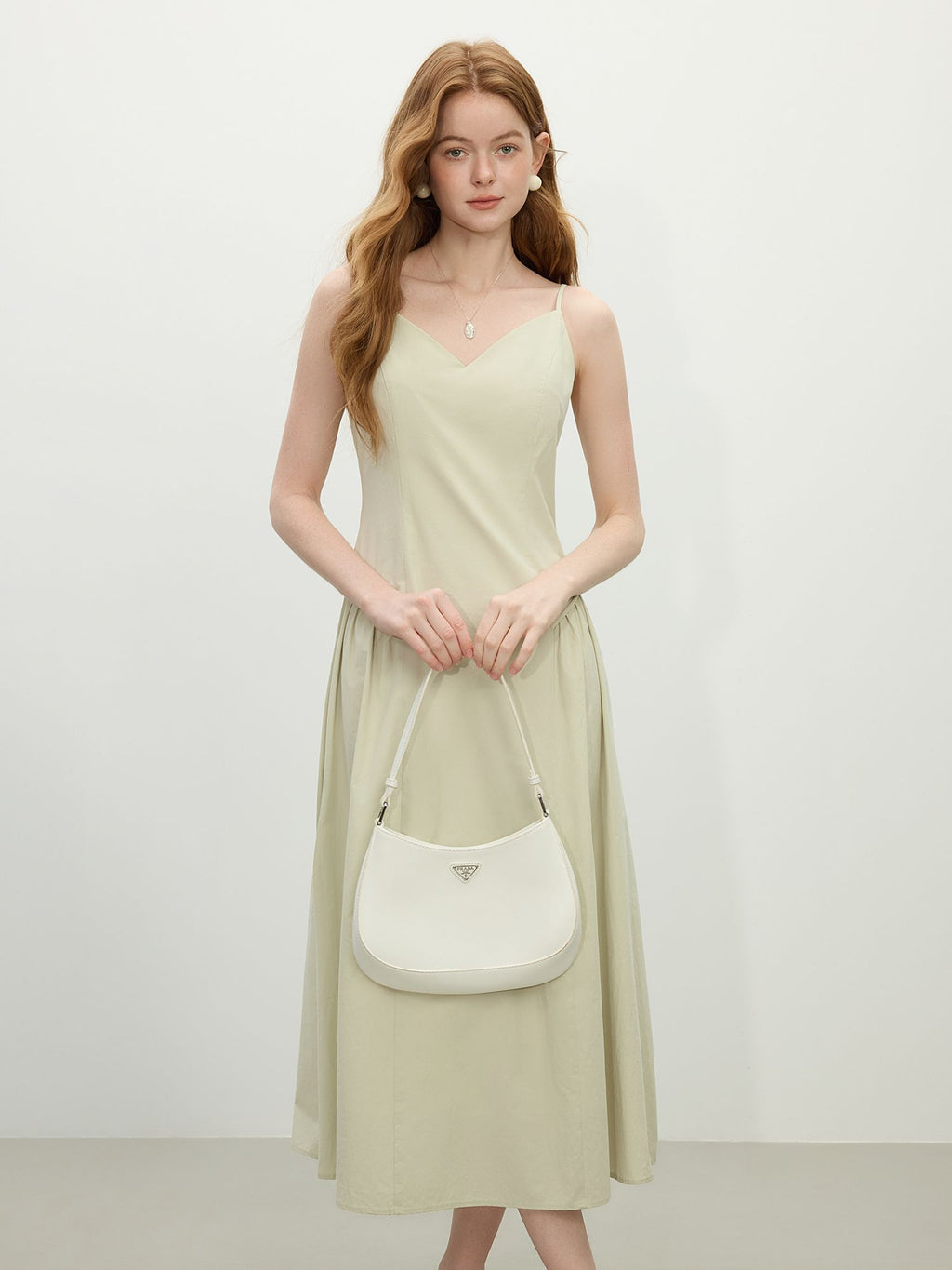 Modell trägt hellgrünes Midikleid mit Spaghettiträgern und V-Ausschnitt, kombiniert mit weißer Schultertasche