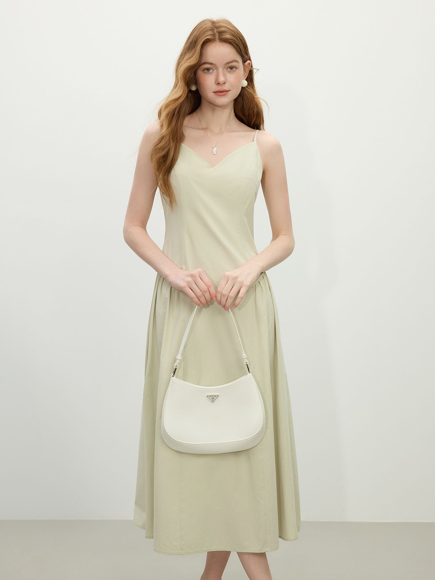 Modell trägt hellgrünes Midikleid mit Spaghettiträgern und V-Ausschnitt, kombiniert mit weißer Schultertasche