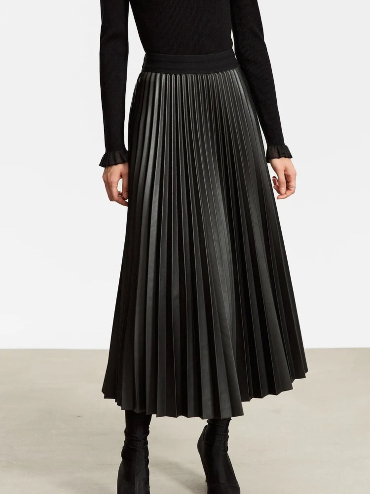 Close-up of black pleated faux leather skirt with high waist and structured folds