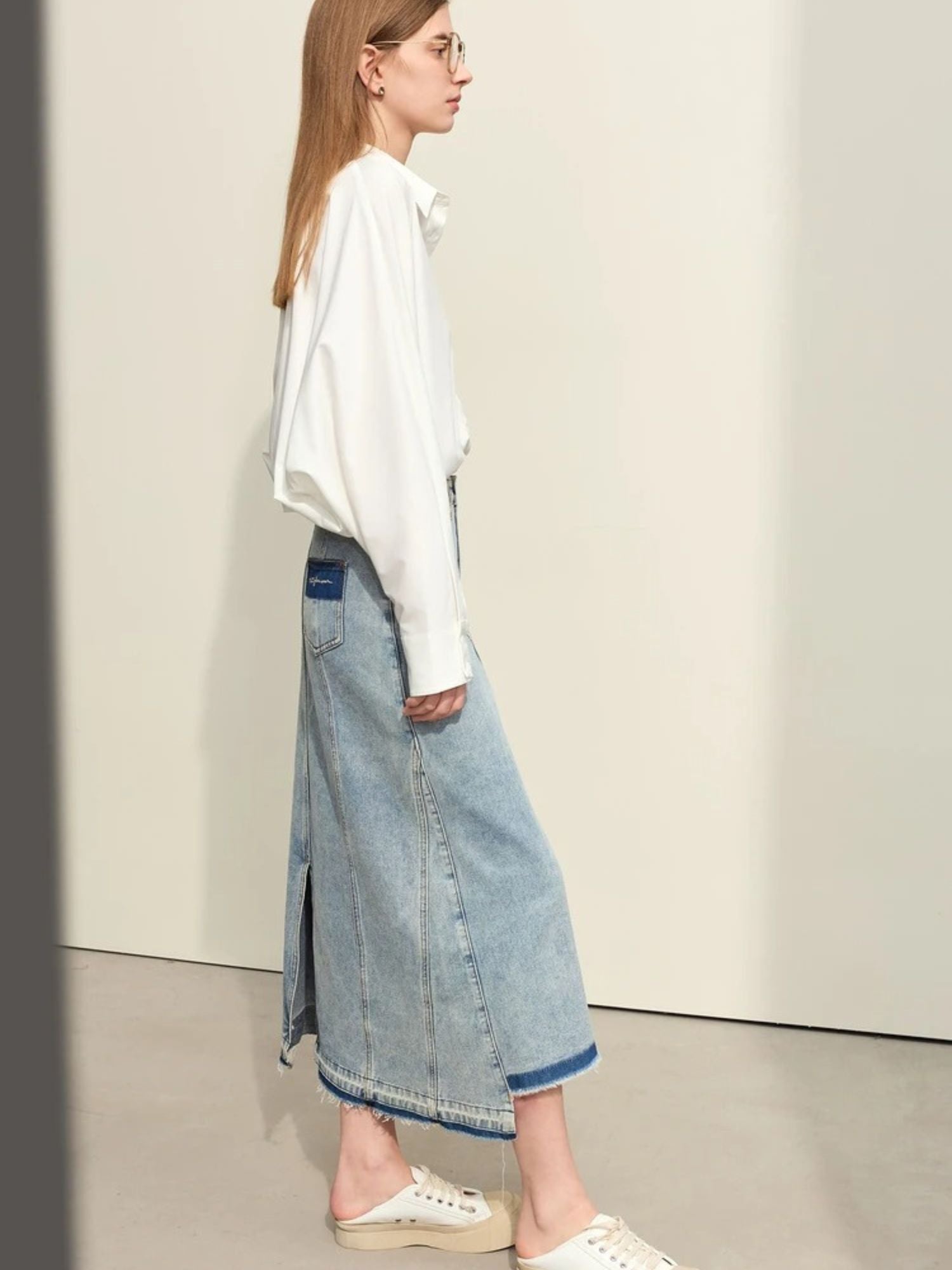 Side profile of light denim skirt with front slit, worn with white sweatshirt
