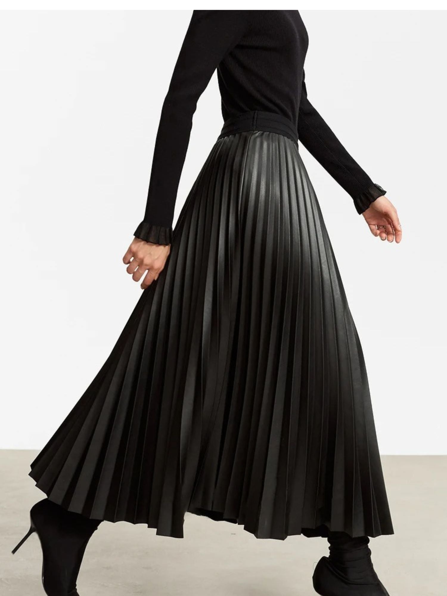 Side view of black pleated skirt in motion, styled with black knit top