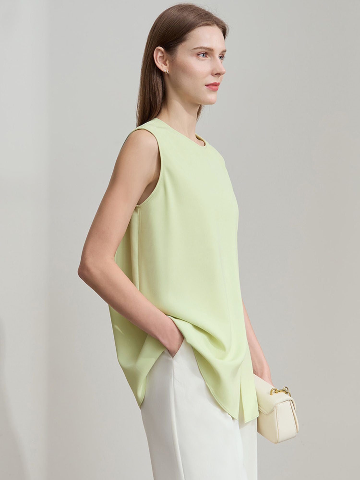Frau steht seitlich und trägt hellgrüne ärmellose Bluse mit Faltenwurf