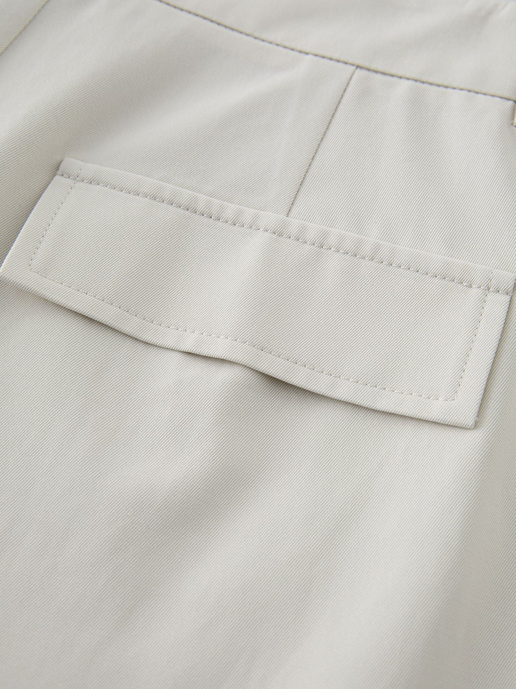 Detailansicht der Gesäßtasche mit feiner Naht auf cremefarbenem Stoff