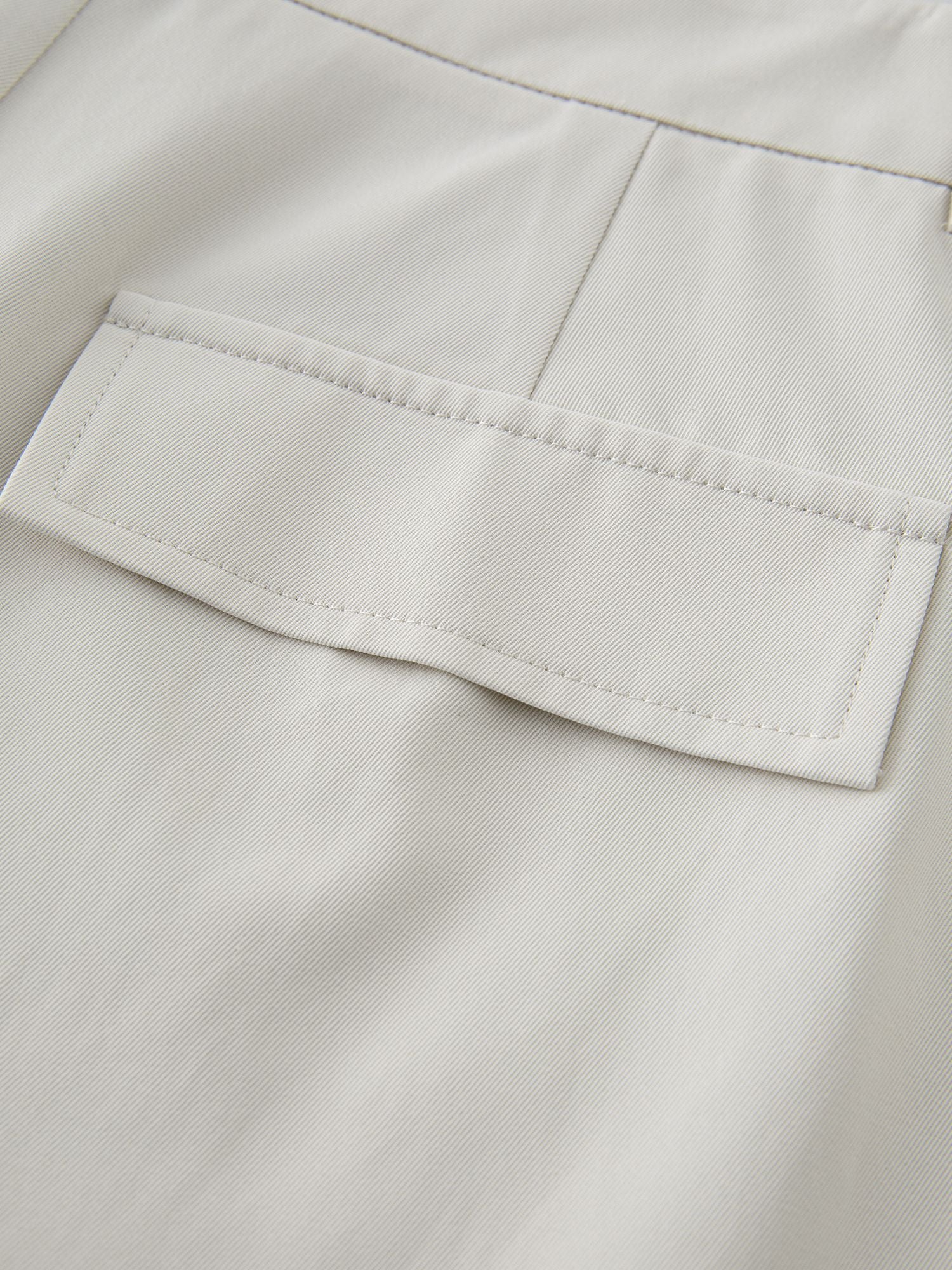 Detailansicht der Gesäßtasche mit feiner Naht auf cremefarbenem Stoff