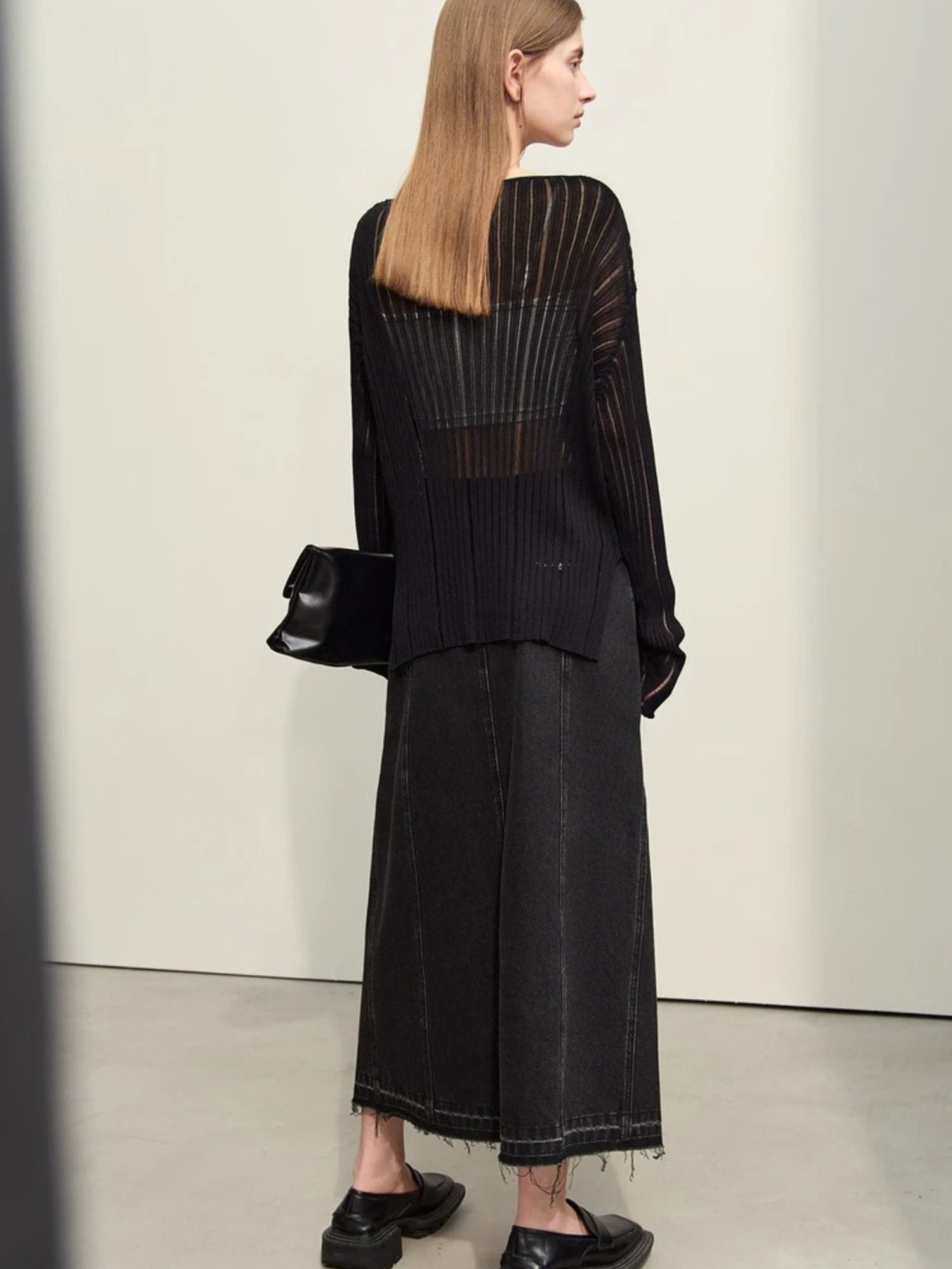 Side view of black midi skirt with flared silhouette and loafers