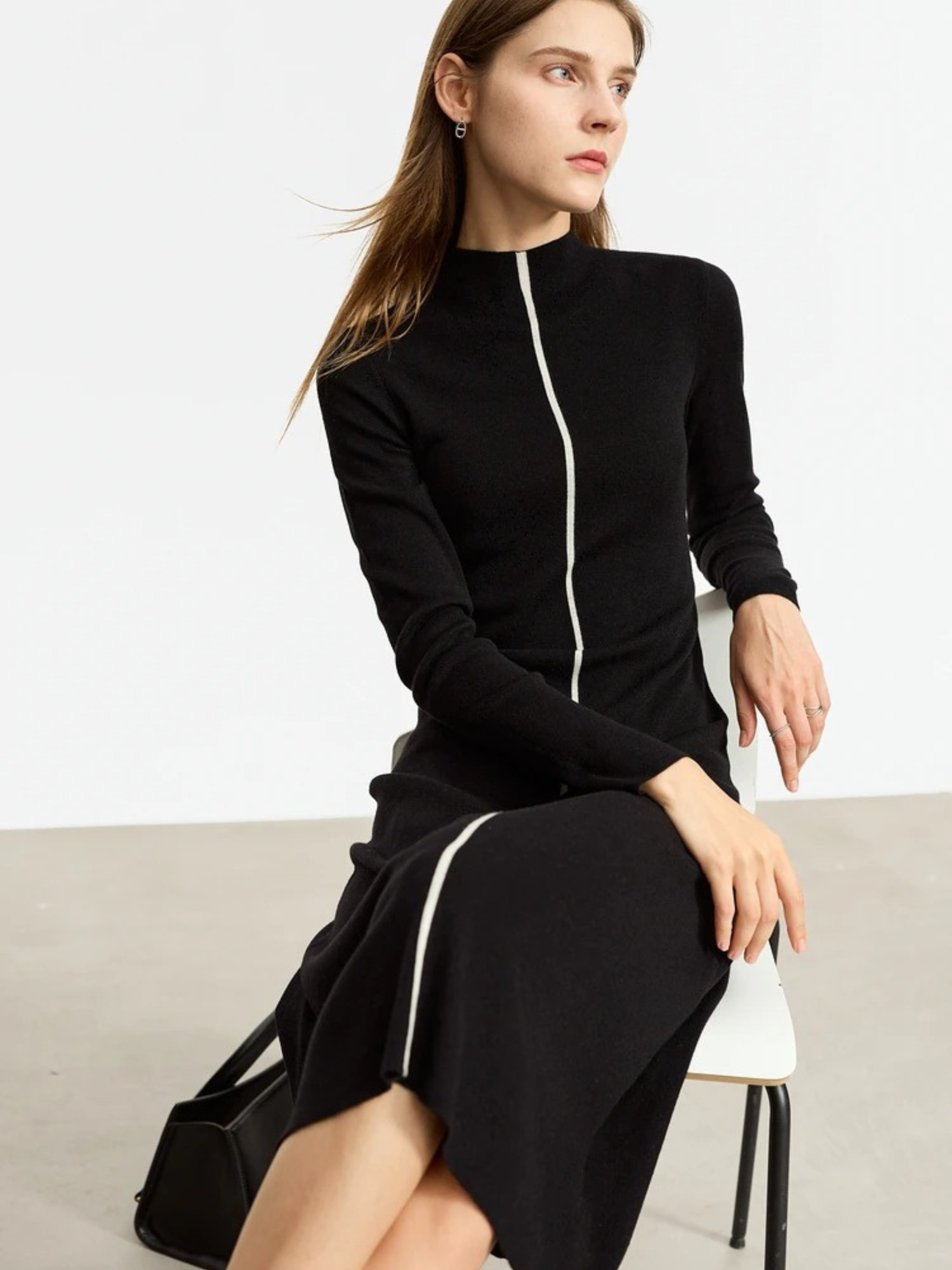 Black knit dress with front zipper, worn seated and styled with crossbody bag