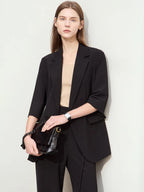 Model holding clutch bag wearing relaxed black blazer and tailored trousers