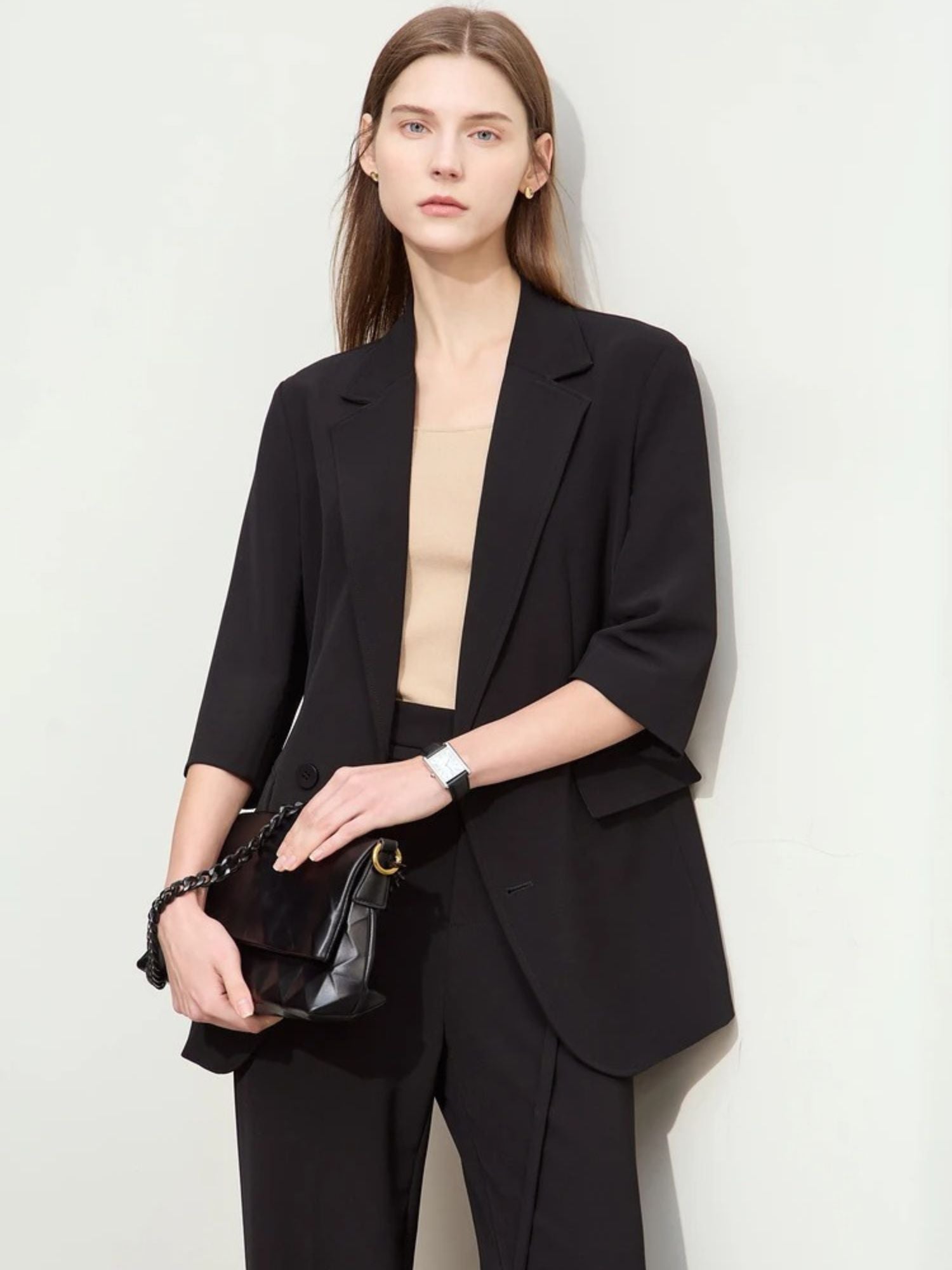 Model holding clutch bag wearing relaxed black blazer and tailored trousers