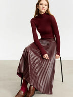 Model seated in burgundy pleated faux leather skirt with long-sleeve turtleneck