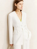 Front view of white belted pantsuit with deep neckline, styled with green inner top