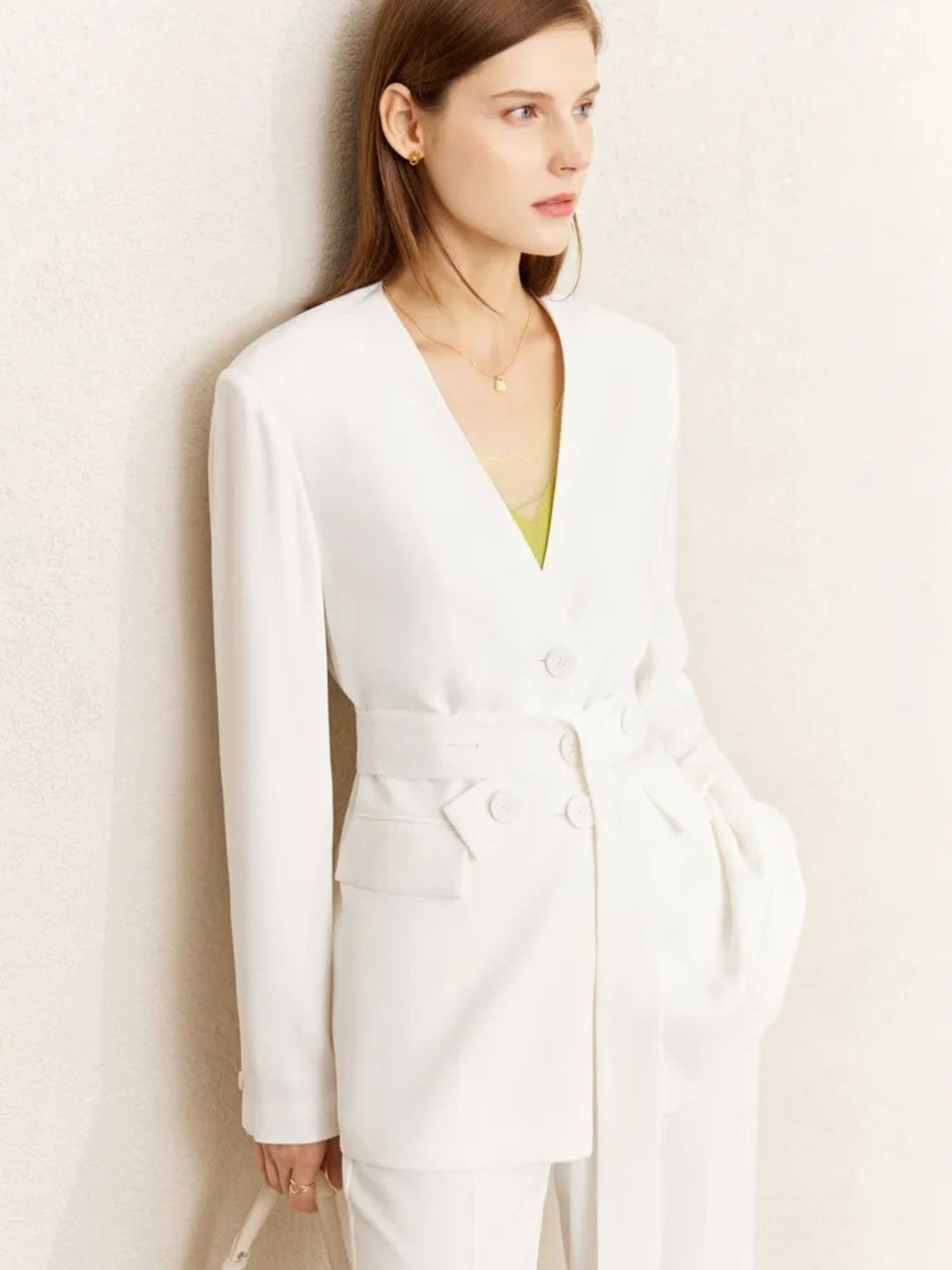 Front view of white belted pantsuit with deep neckline, styled with green inner top