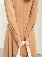 Close-up of camel dress sleeves with gold buttons and gathered cuffs