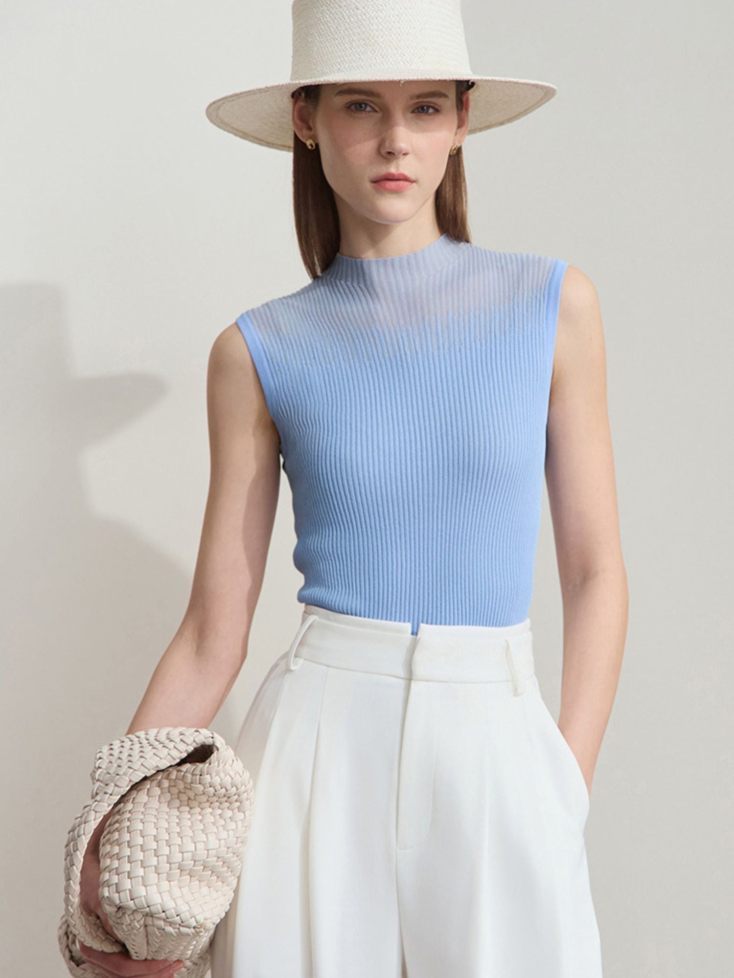 Frau in ärmellosem blauen Stricktop und weißer Hose mit breitem Sonnenhut